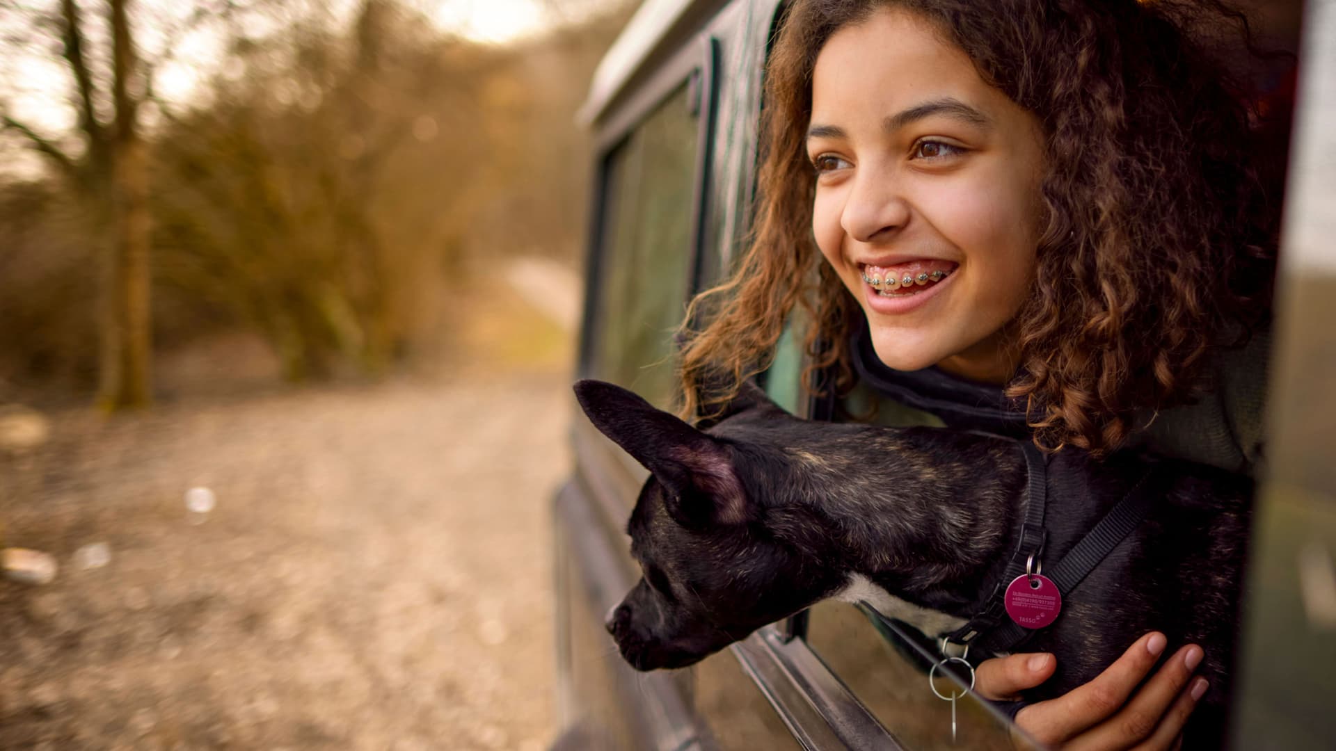 Porträt einer glücklichen Jugendlichen, die mit ihrem Hund aus einem offenen Autofenster schaut.