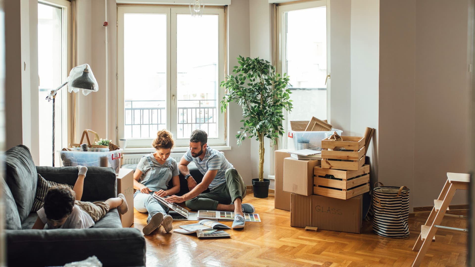 Mann und Frau auf dem Boden mit Katalog und ein Kind liegend auf der Couch im Wohnzimmer.