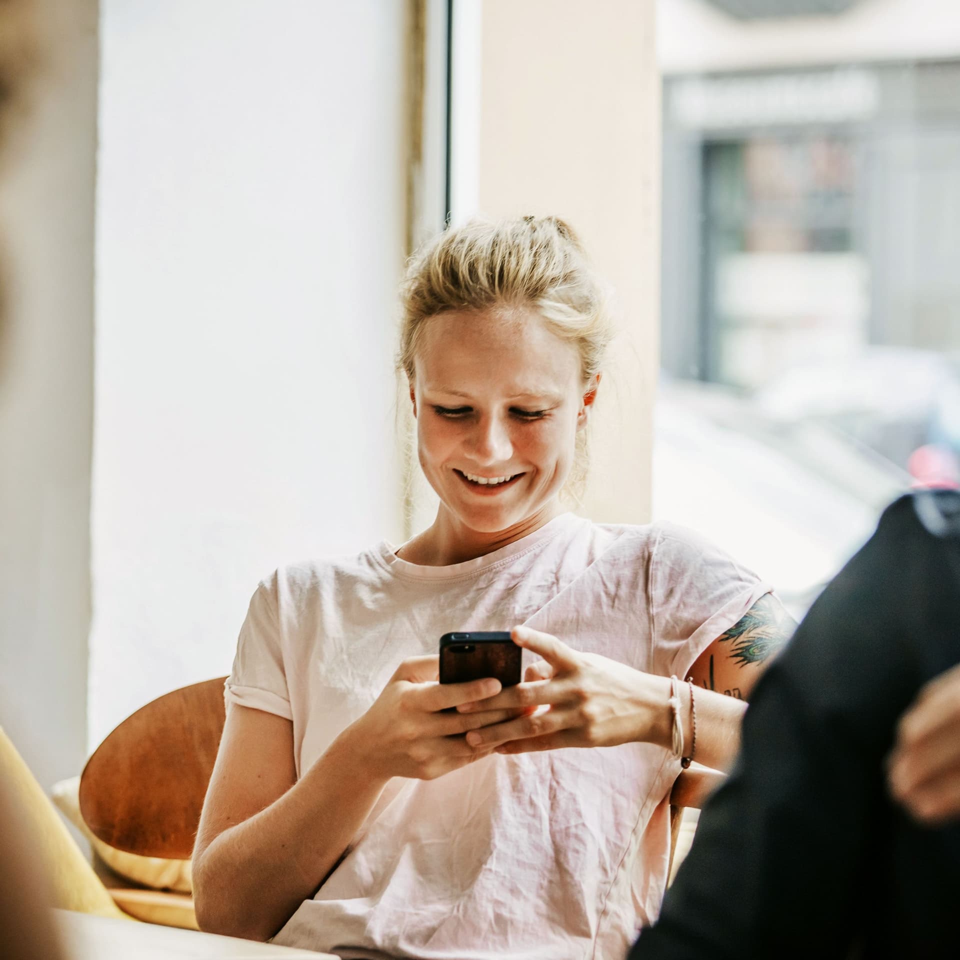 Lächelnde junge Frau sitzt in Café und schaut auf ihr Smartphone.