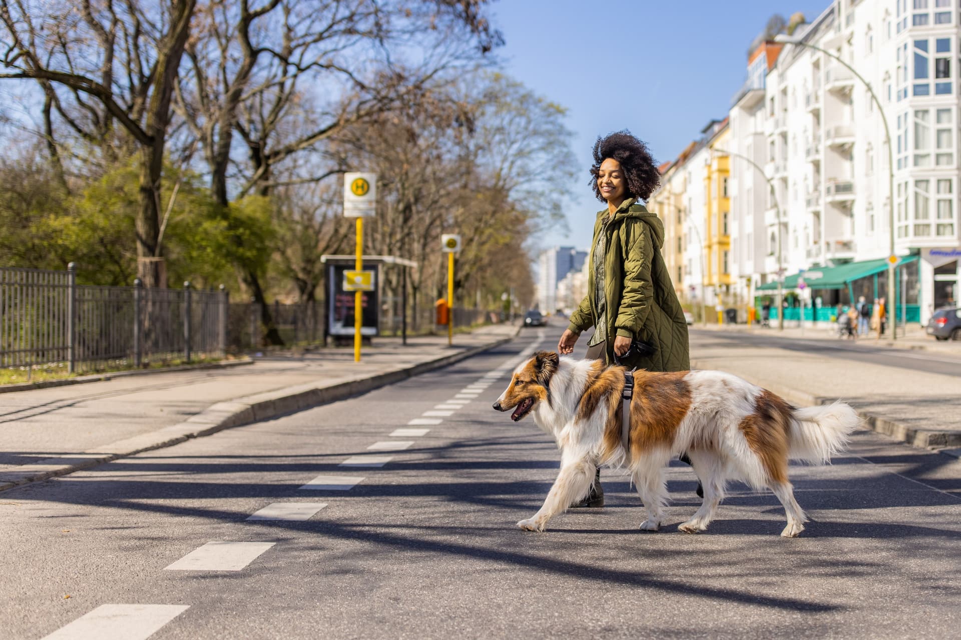 Junge, lächelnde Frau überquert eine Straße mit einem Hund an der Leine.