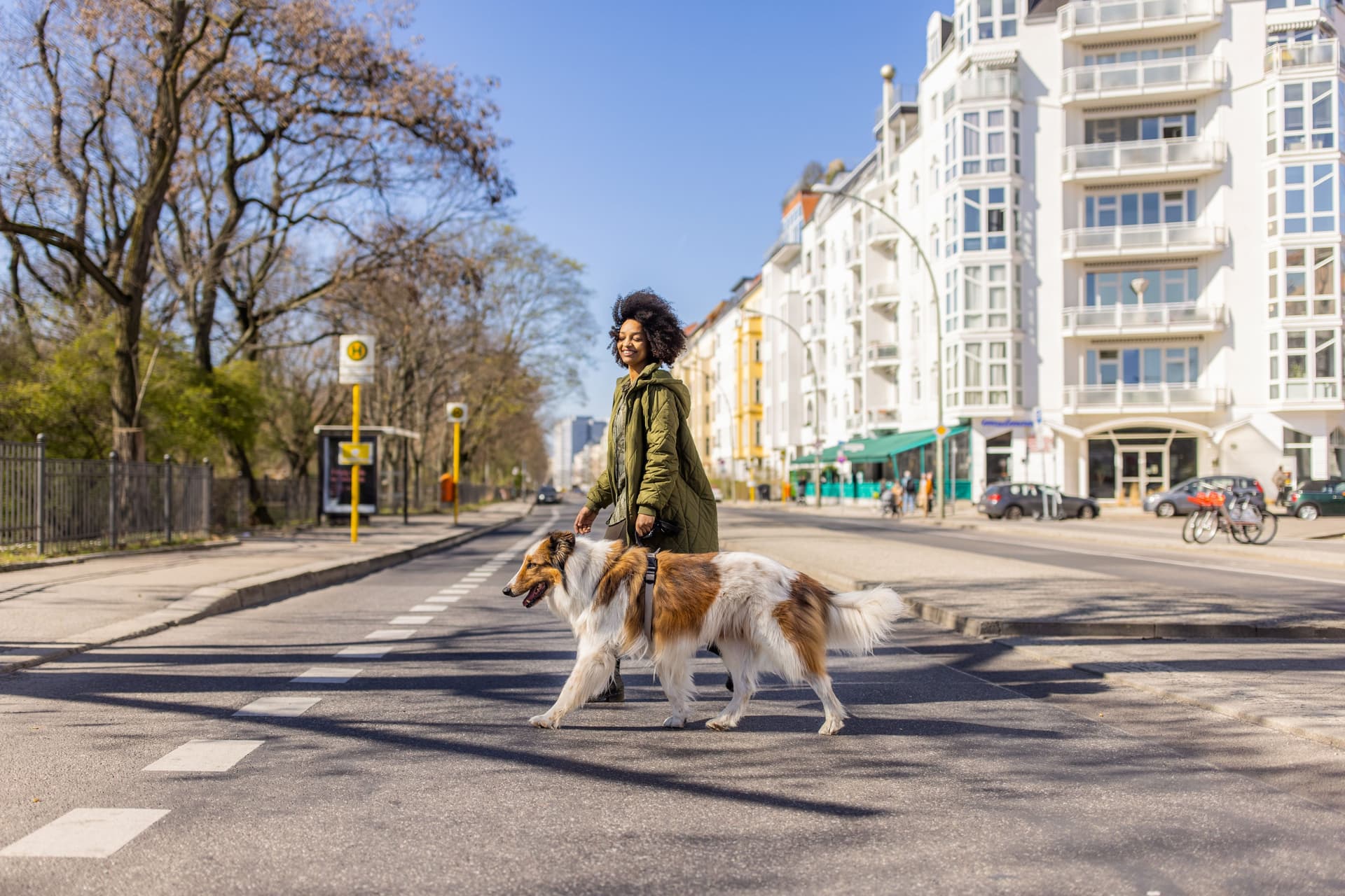 Junge, lächelnde Frau überquert eine Straße mit einem Hund an der Leine.