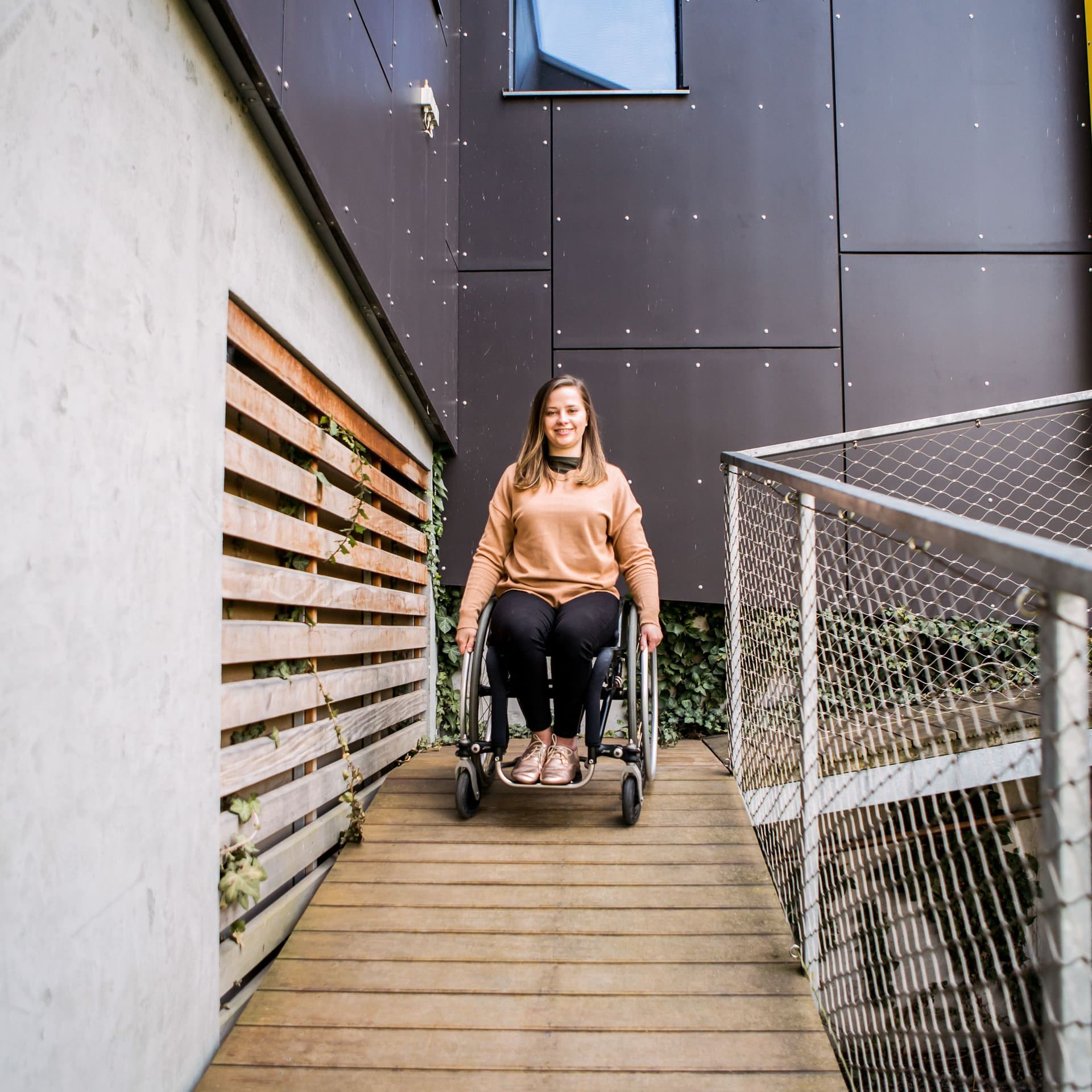 Junge Frau im Rollstuhl, die eine Rampe runterfährt.