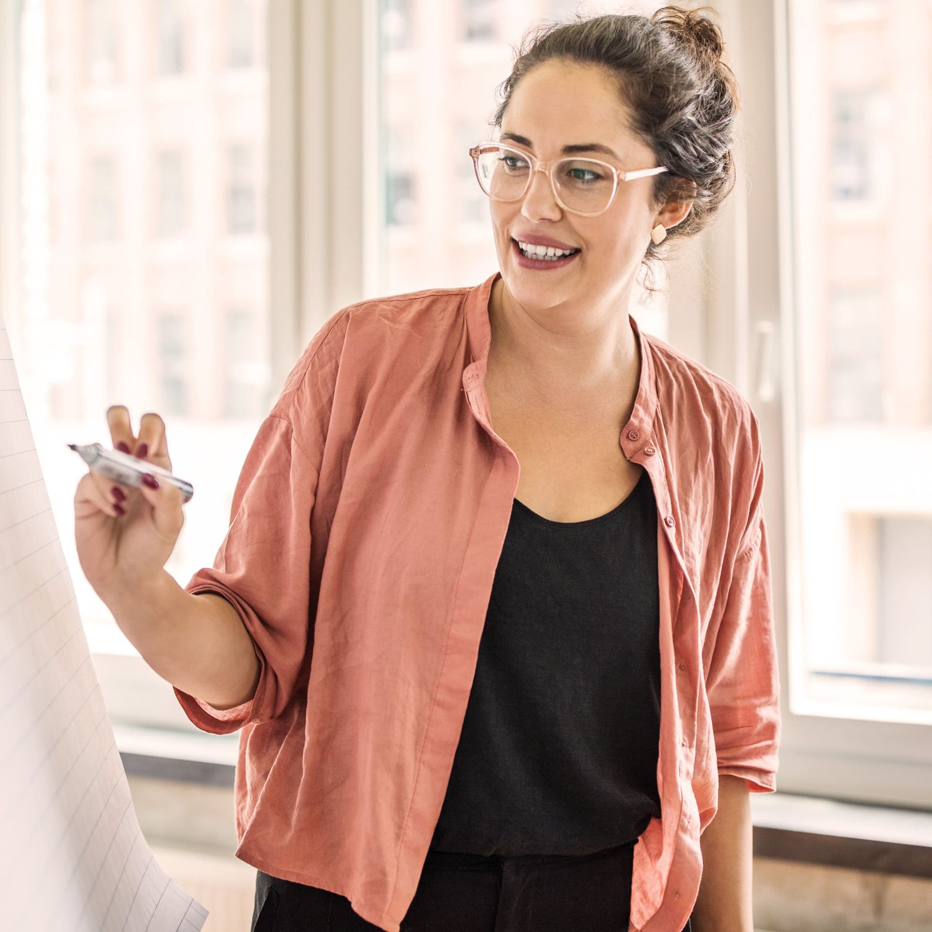 Junge Frau schreibt während einer Präsentation auf ein Flipchart. Sie lächelt dabei.