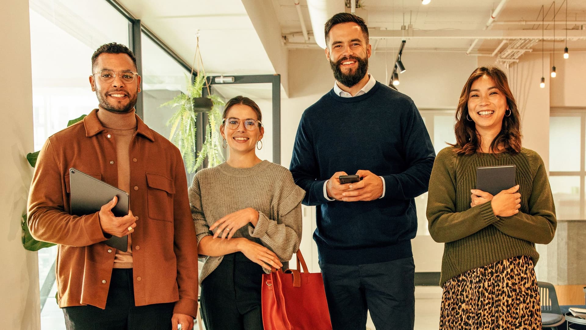 Zwei Frauen und zwei Männer stehen lächelnd in einem modern eingerichteten Büro.