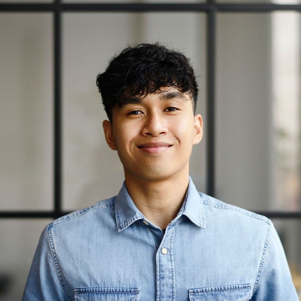 Portrait von einem jungen Mann, der in einem modernen und offenen Büro steht und in die Kamera lächelt.