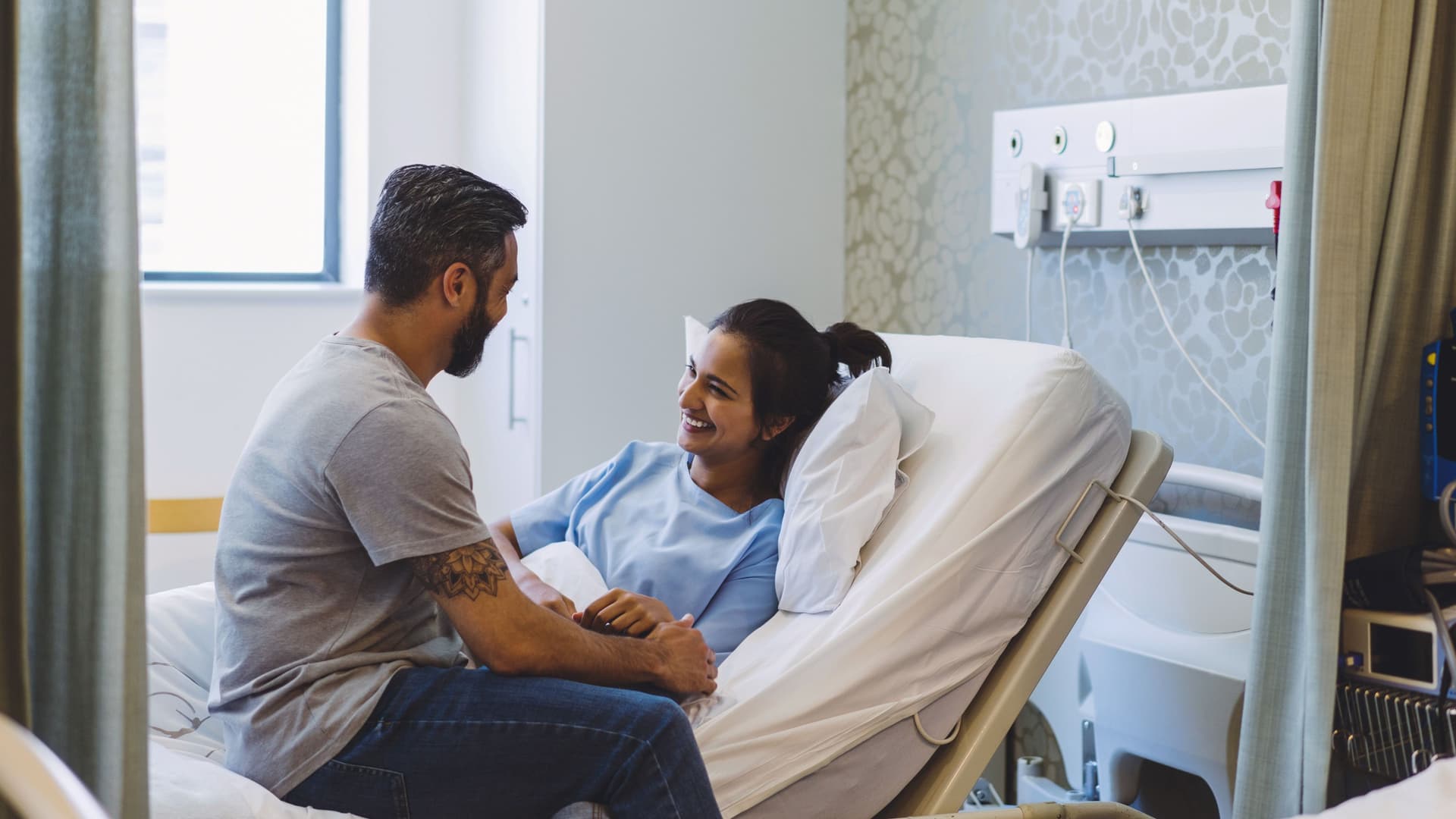 Mann sitzt mit kranker Patientin auf ihrem Bett im Krankenhaus