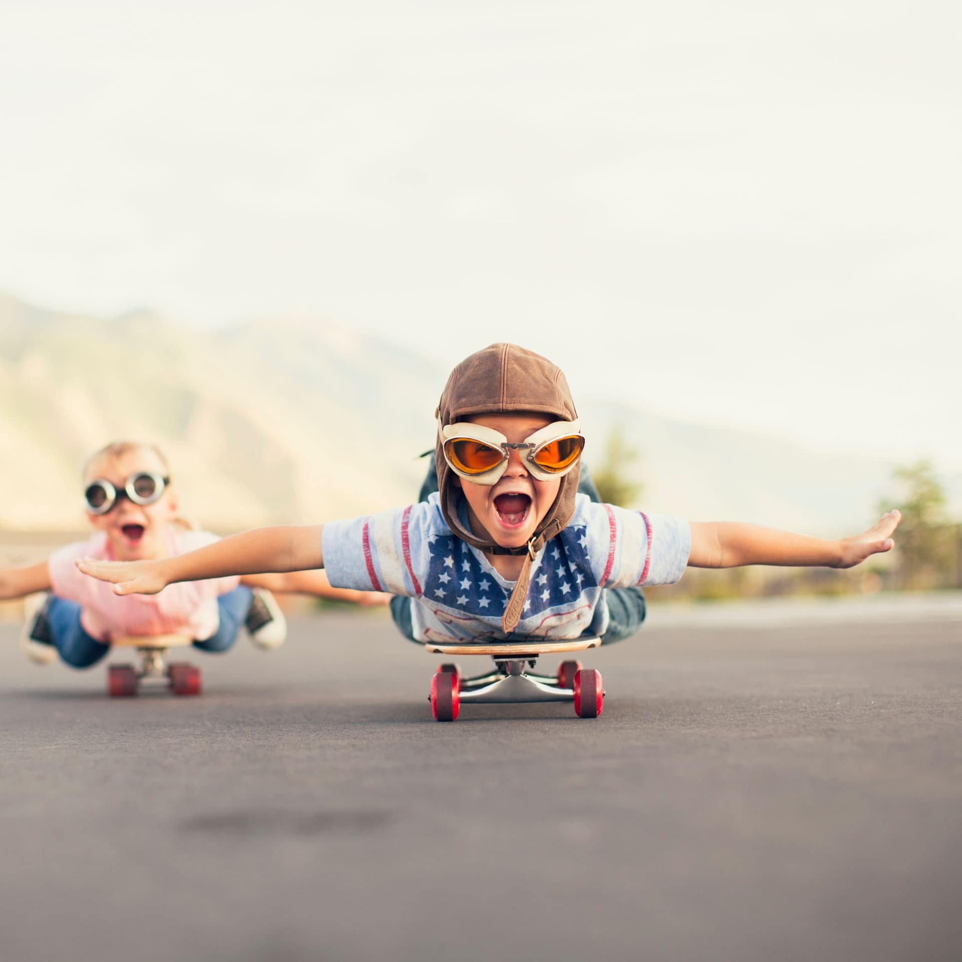 Zwei Kinder fahren bäuchlings auf einem Skateboard und strecken dabei die Arme aus als ob sie fliegen würden.