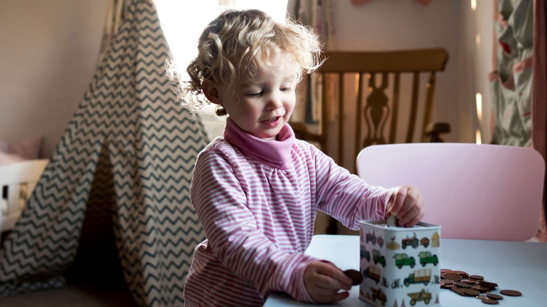 Kleinkind im Kinderzimmer steckt Münzen in eine Spardose