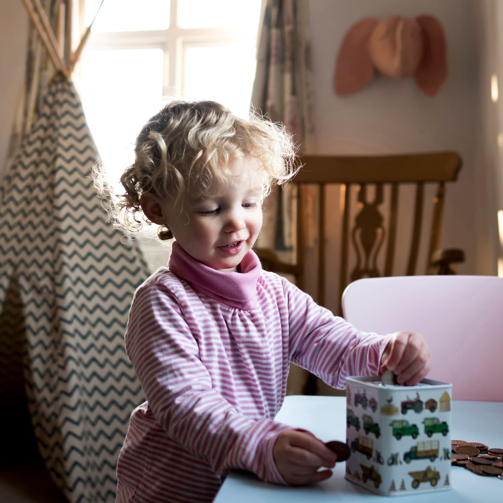 Kleinkind im Kinderzimmer steckt Münzen in eine Spardose