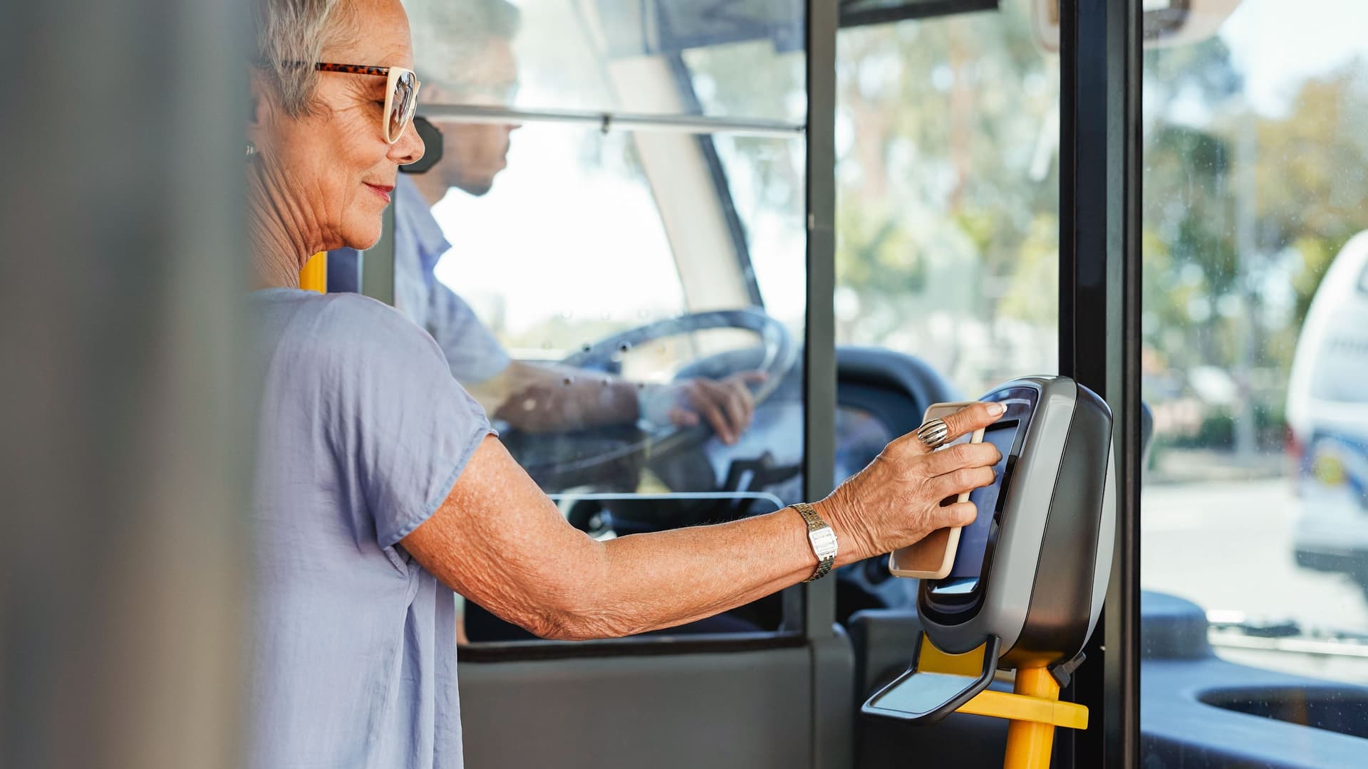Eine Seniorin steht im Einstiegsbereich eines Busses und bezahlt mit ihrem Smartphone am Lesegerät.