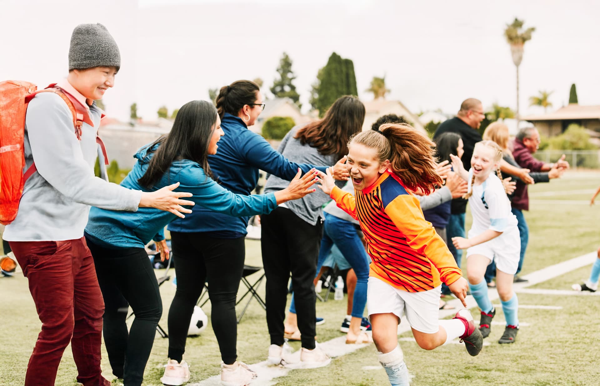Mädchen in Fußballtrikots klatschen jubelnd auf einem Fußballplatz mit den am Rande stehenden Frauen und Männern ab.
