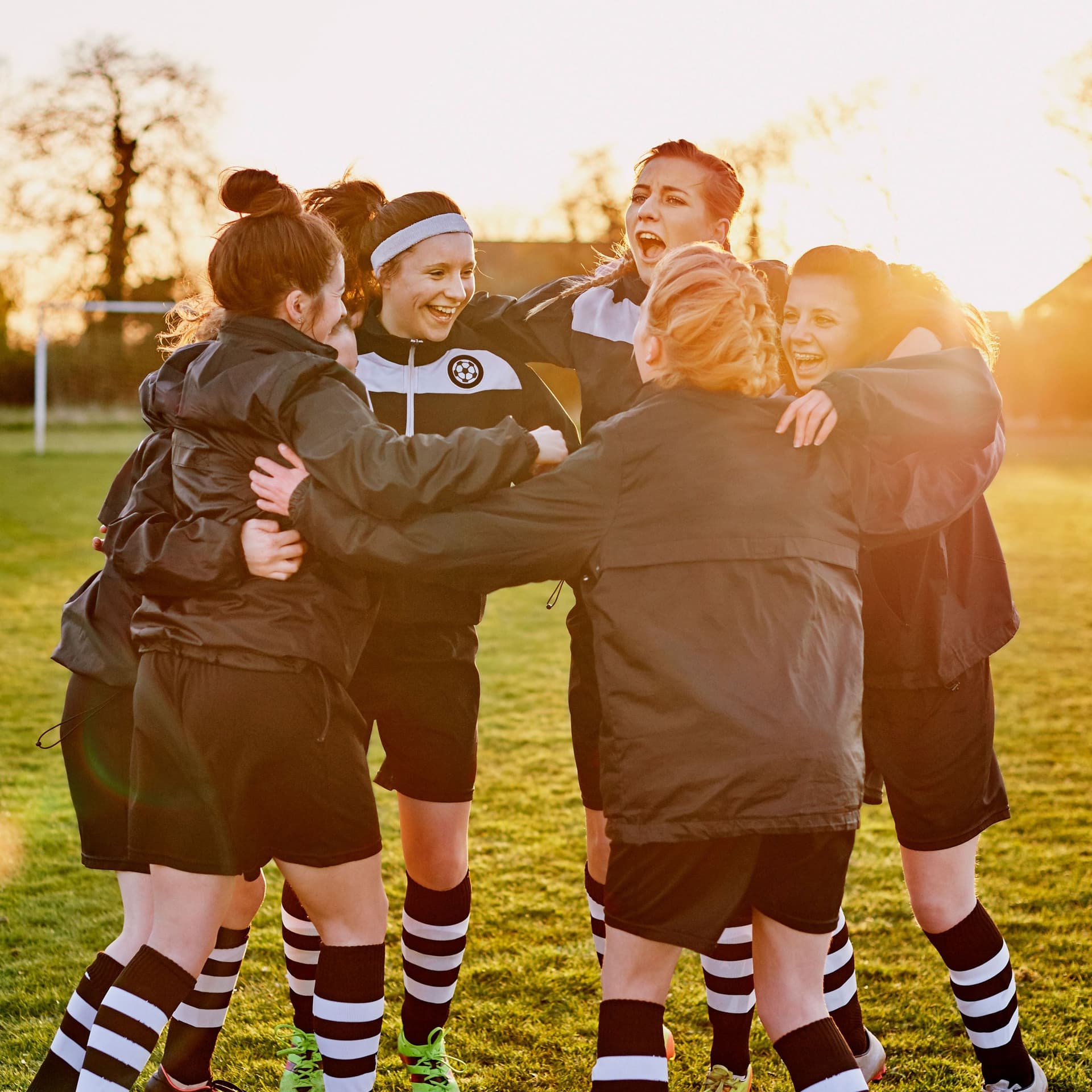 Junge Frauen im Trikot stehen auf einem Fussballplatz im Kreis. Sie halten sich an den Schultern