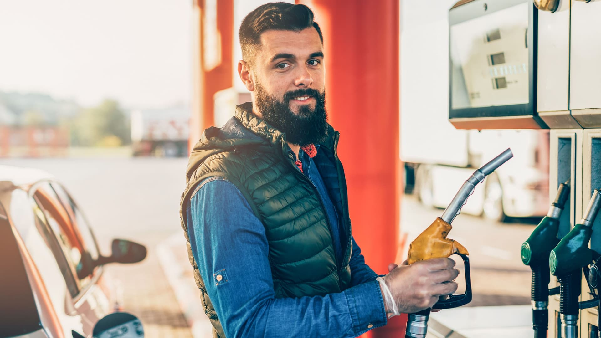 Junger Mann an einer Tankstelle. Er hält eine Zapfschlauch in der Hand.
