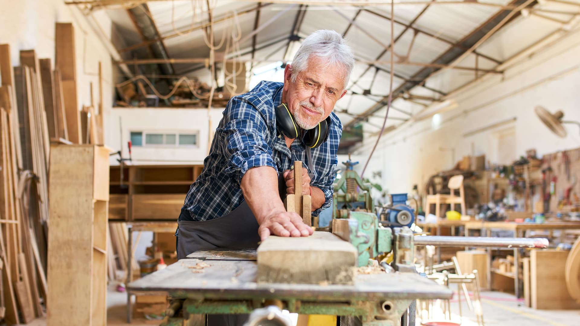 Ein älterer Handwerker arbeitet an der Hobelmaschine in der Werkstatt einer Tischlerei.