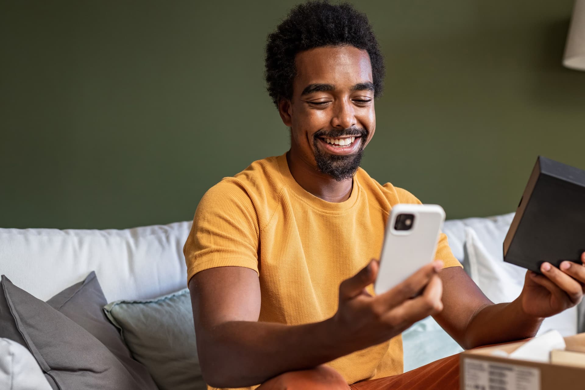 Mann sitzt auf Sofa und freut sich über ein Smartphone, das er gerade auspackt.