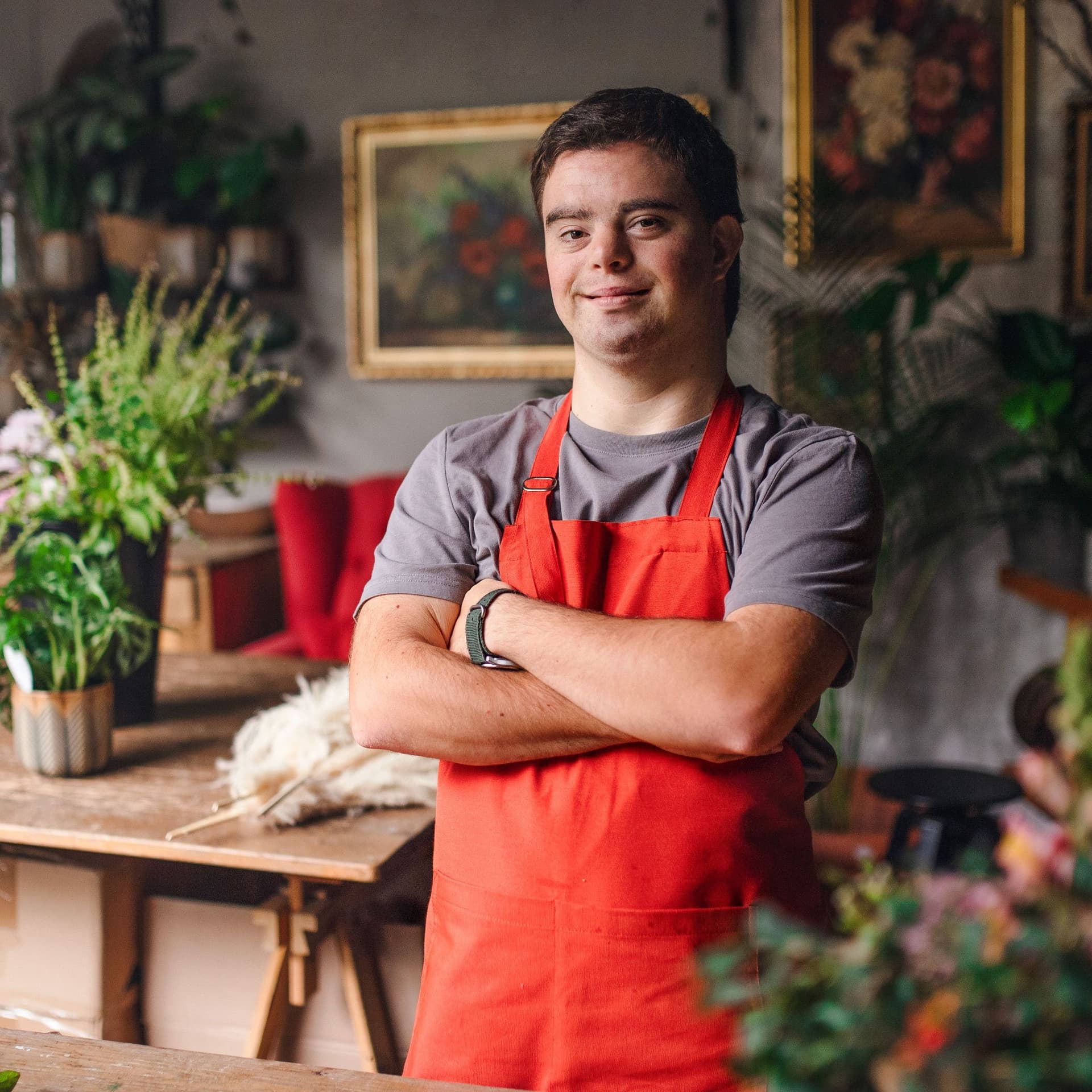 Junger Florist mit Down-Syndrom steht in einem Blumenladen, schaut in die Kamera und lächelt.