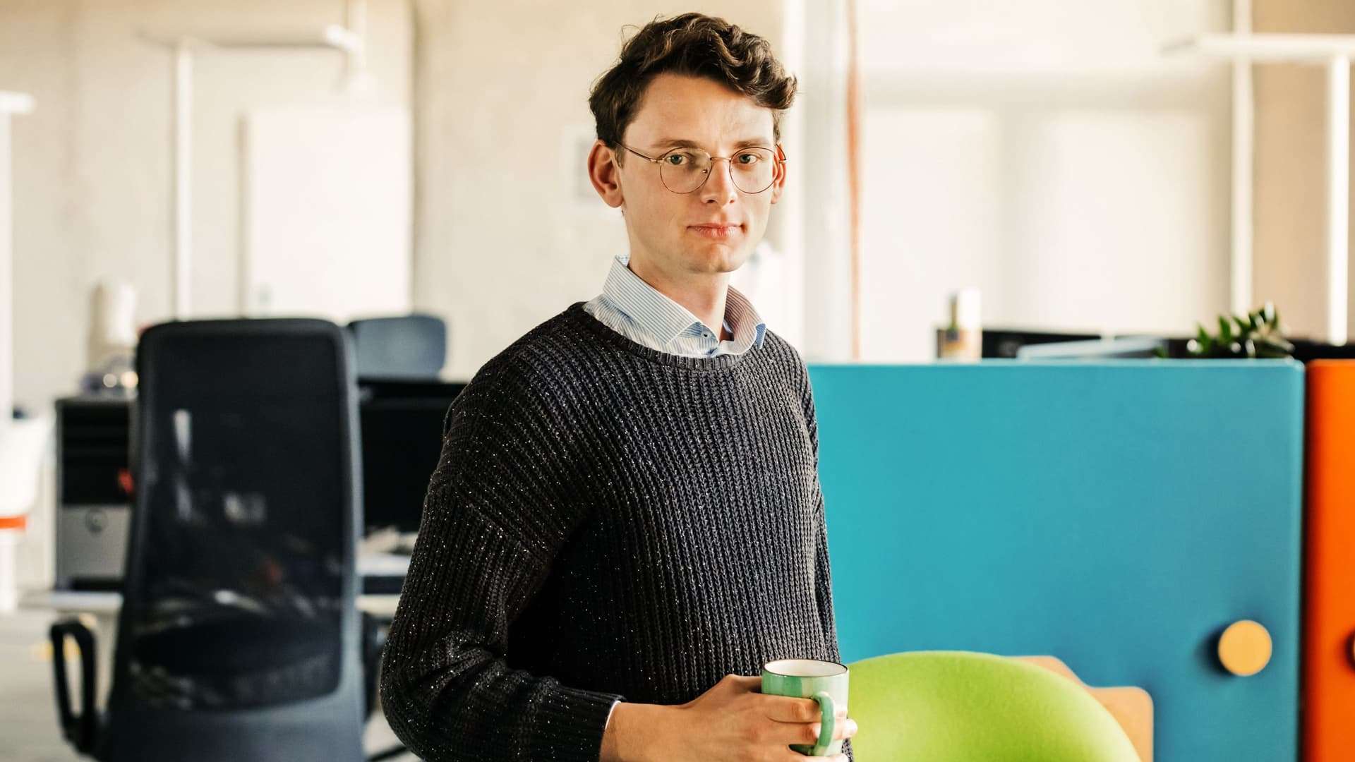 Porträt eines Mitarbeiters im Büro. Im Hintergrund Bürostühle und Computer.