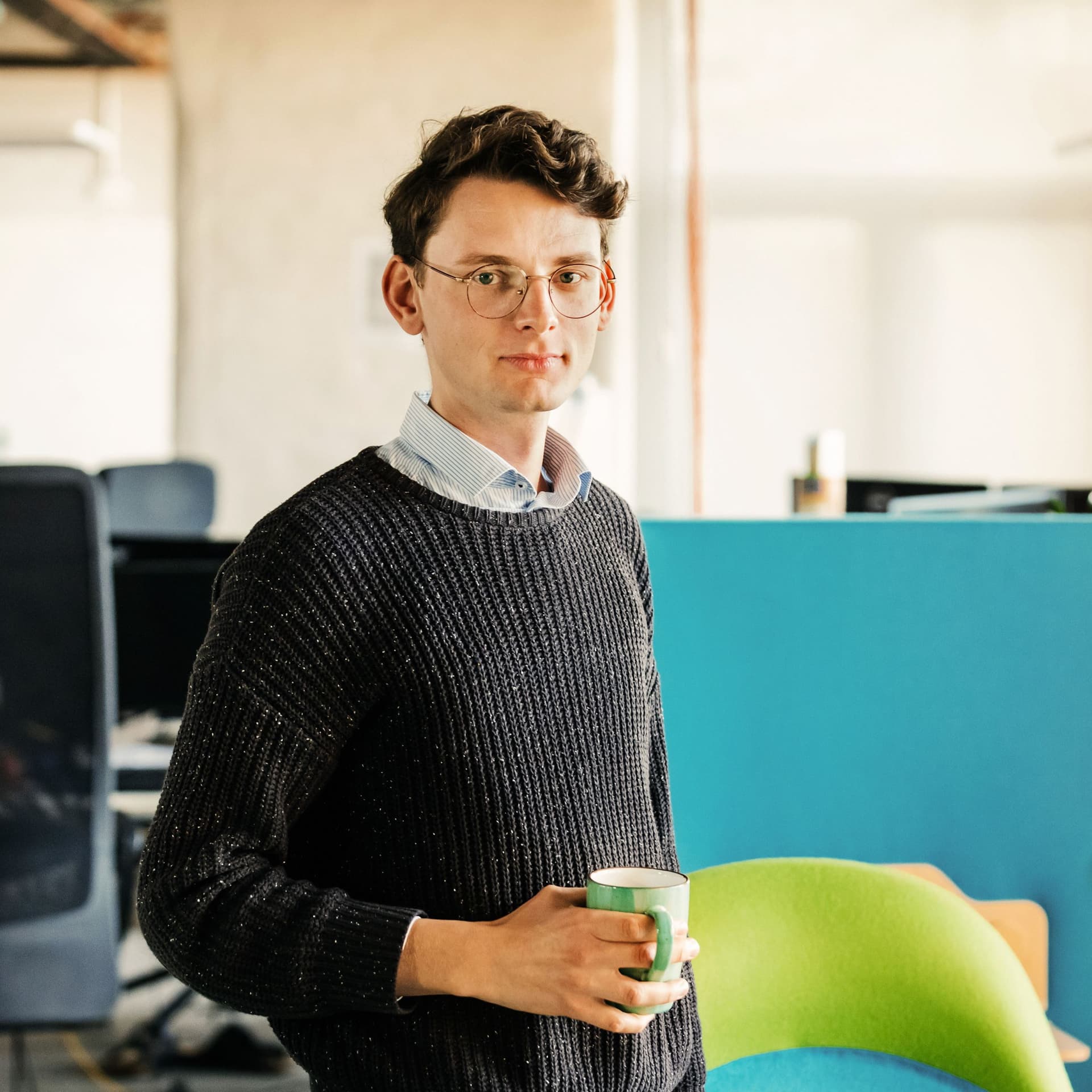 Porträt eines Mitarbeiters im Büro. Im Hintergrund Bürostühle und Computer.