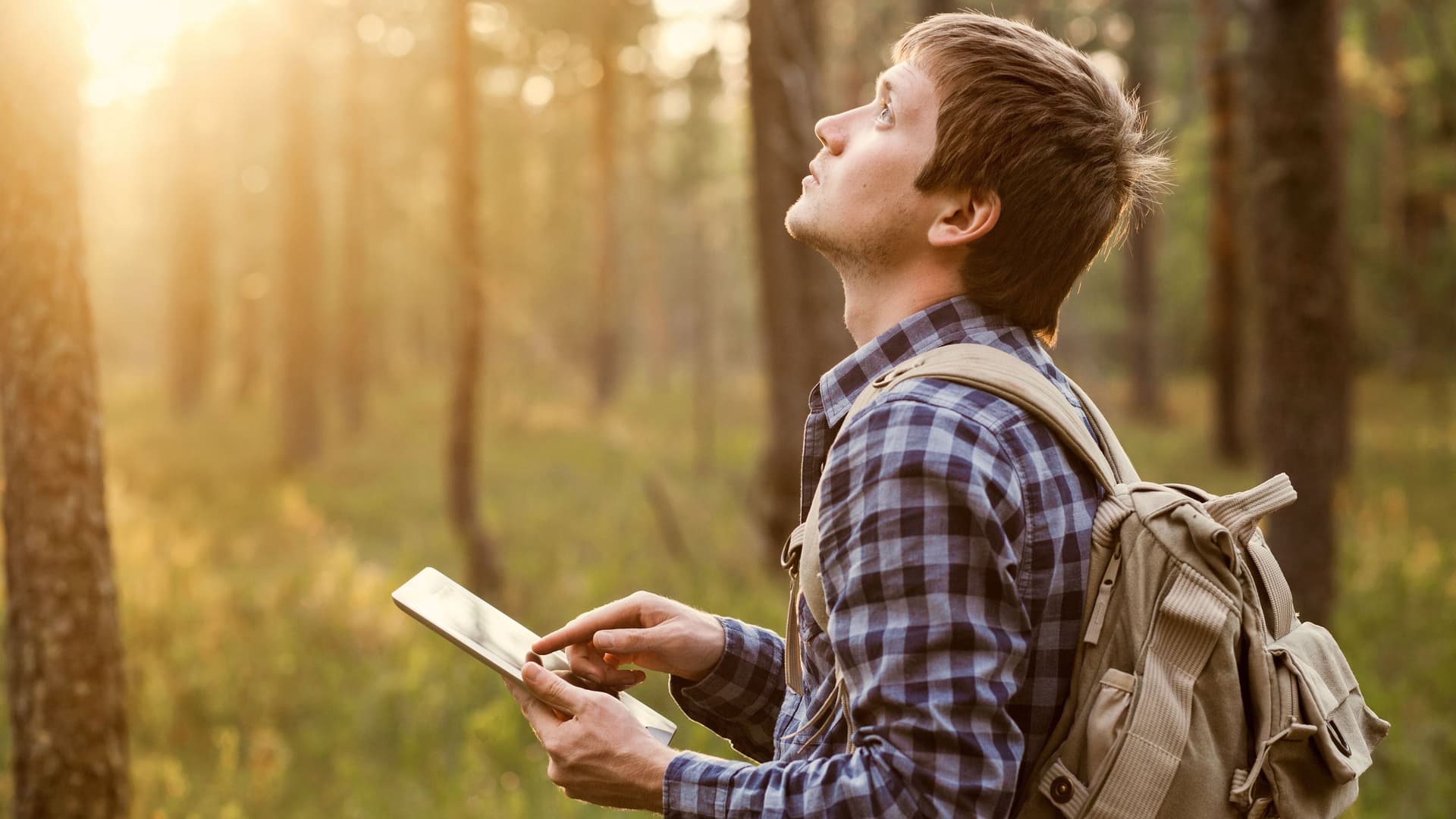 Junger Mann mit Tablet in der Hand wandert durch einen Wald