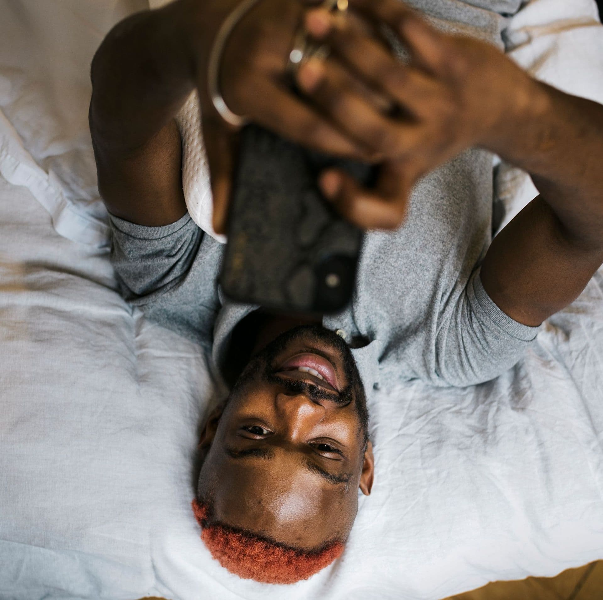 Mann liegt im Bett mit Handy in der Hand von oben