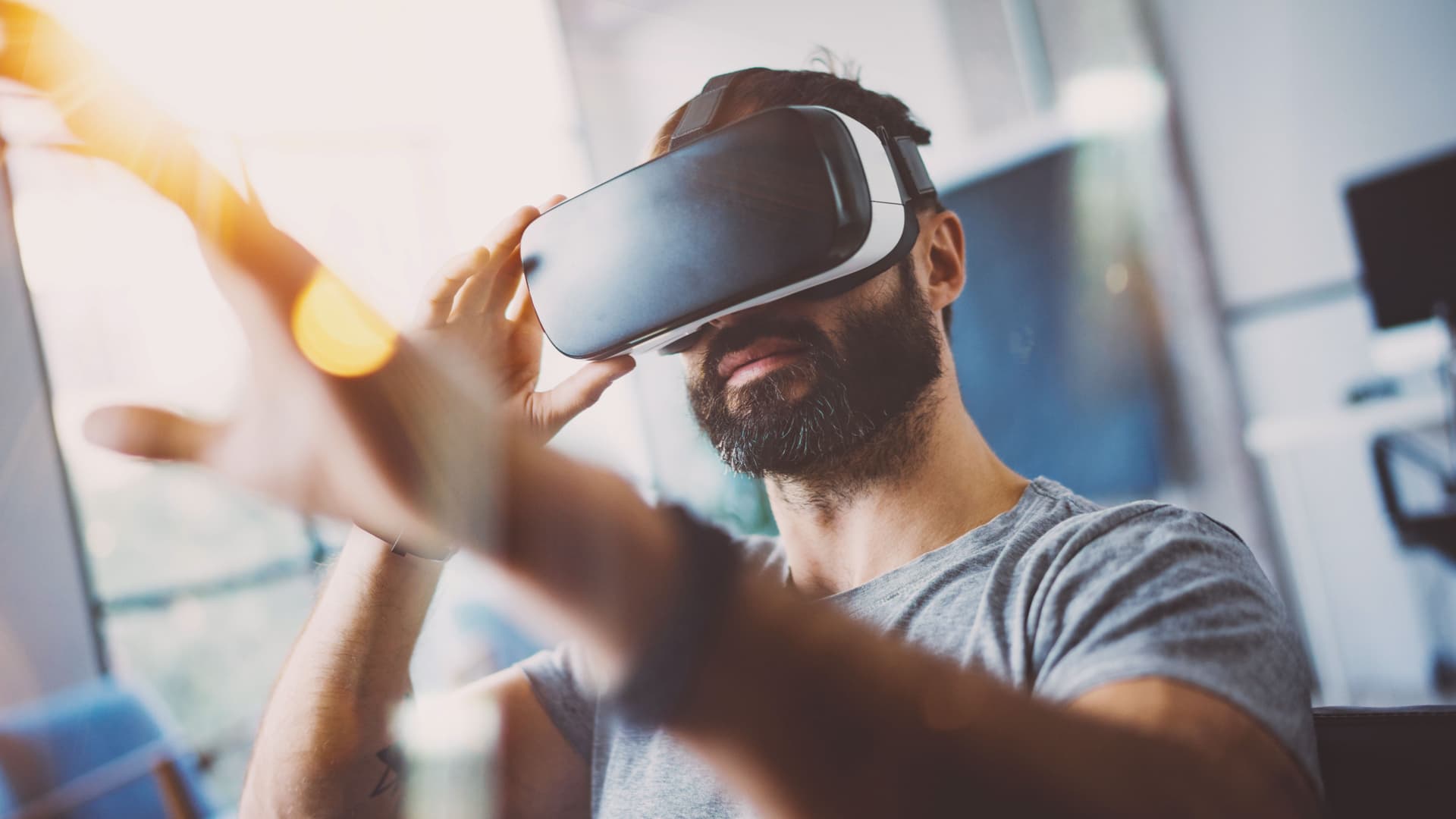 Porträt eines bärtigen Mannes der eine VR Brille trägt und die Hände von sich streckt.