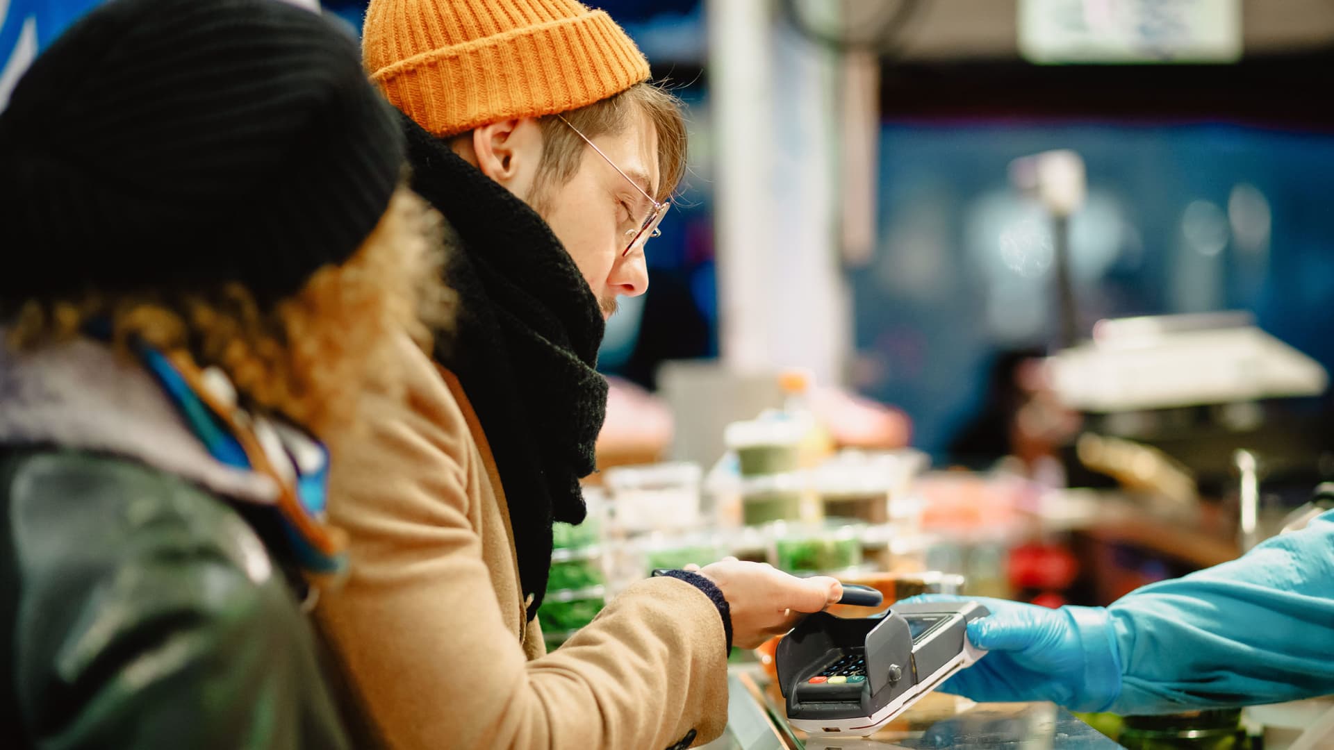 Junger mann mit Beanie zahlt mit seinem Handy in einem Geschäft.