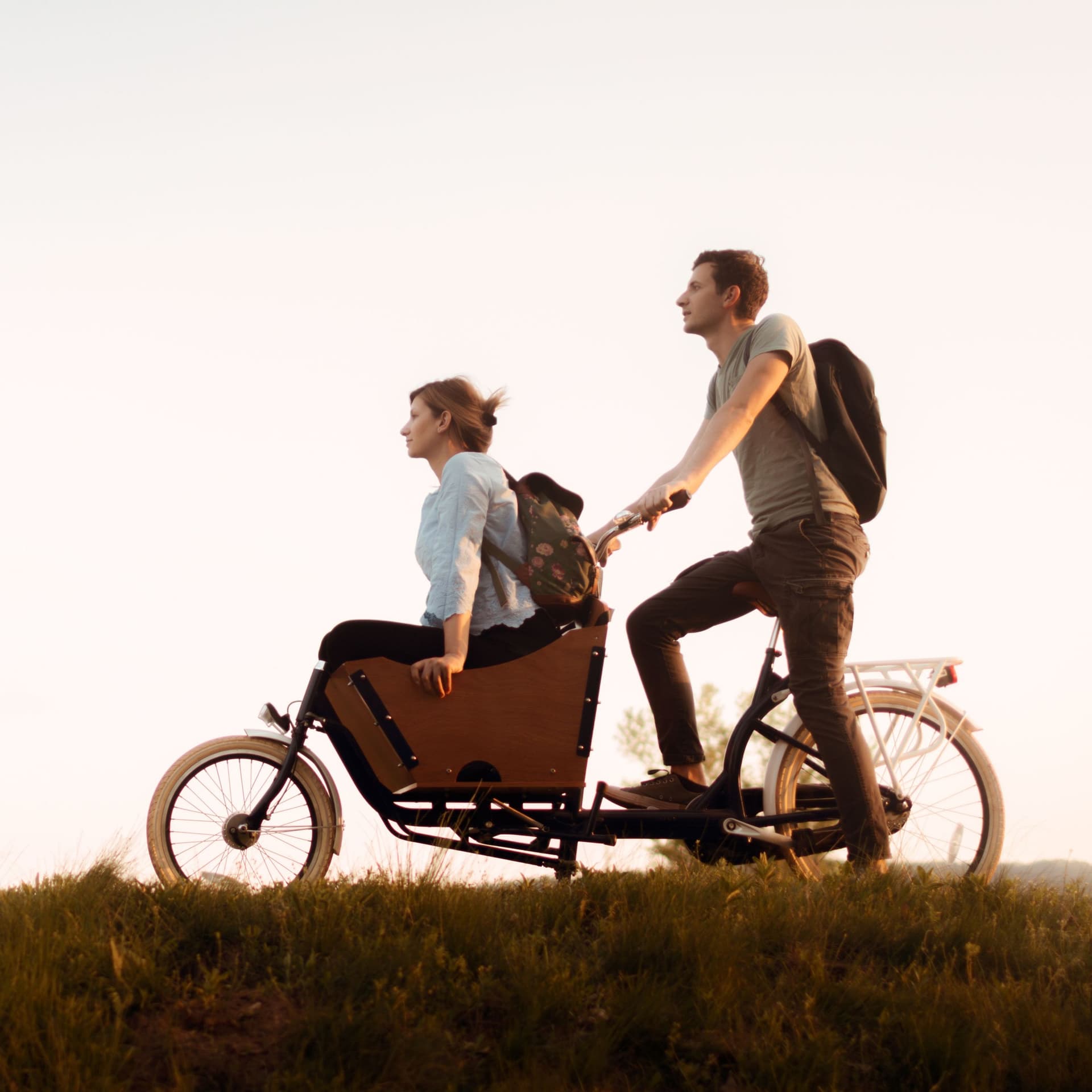 Ein Mann kutschiert eine Frau in einem Lastenrad auf einem Feldweg.