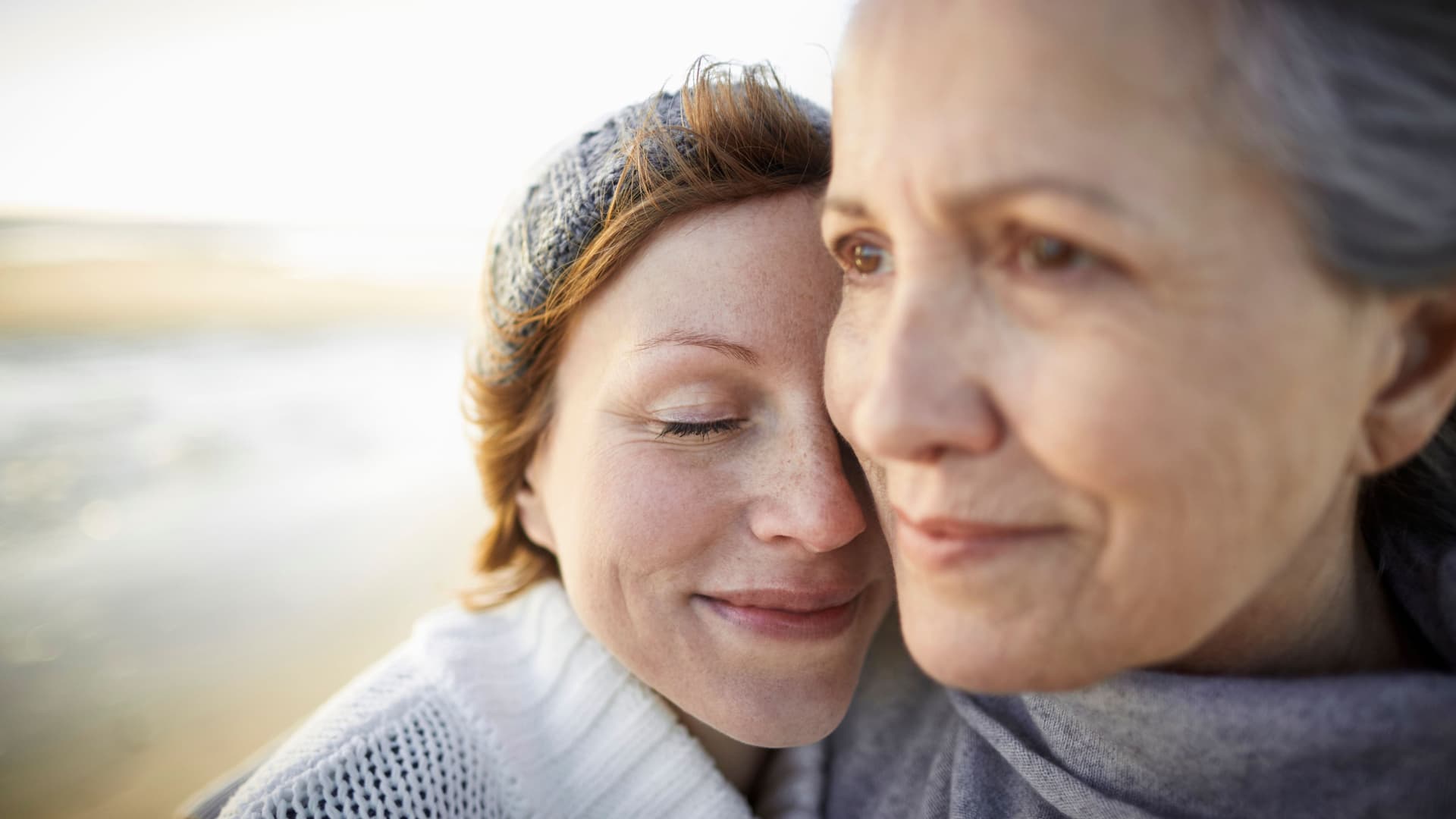 Mutter und erwachsene Tochter am Strand. Sie umarmen sich.
