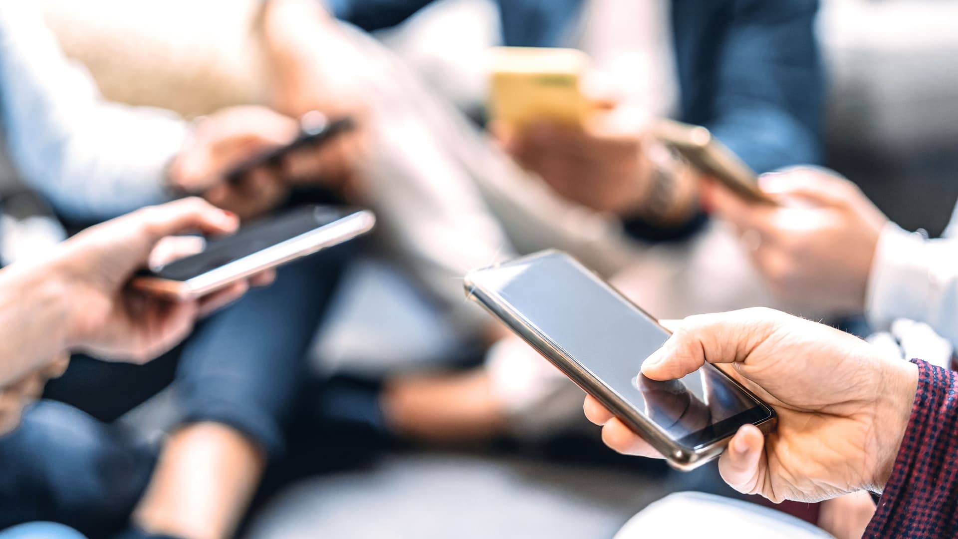 Nahaufnahme von Menschen, die mobile Smartphones benutzen und im Kreis sitzen.