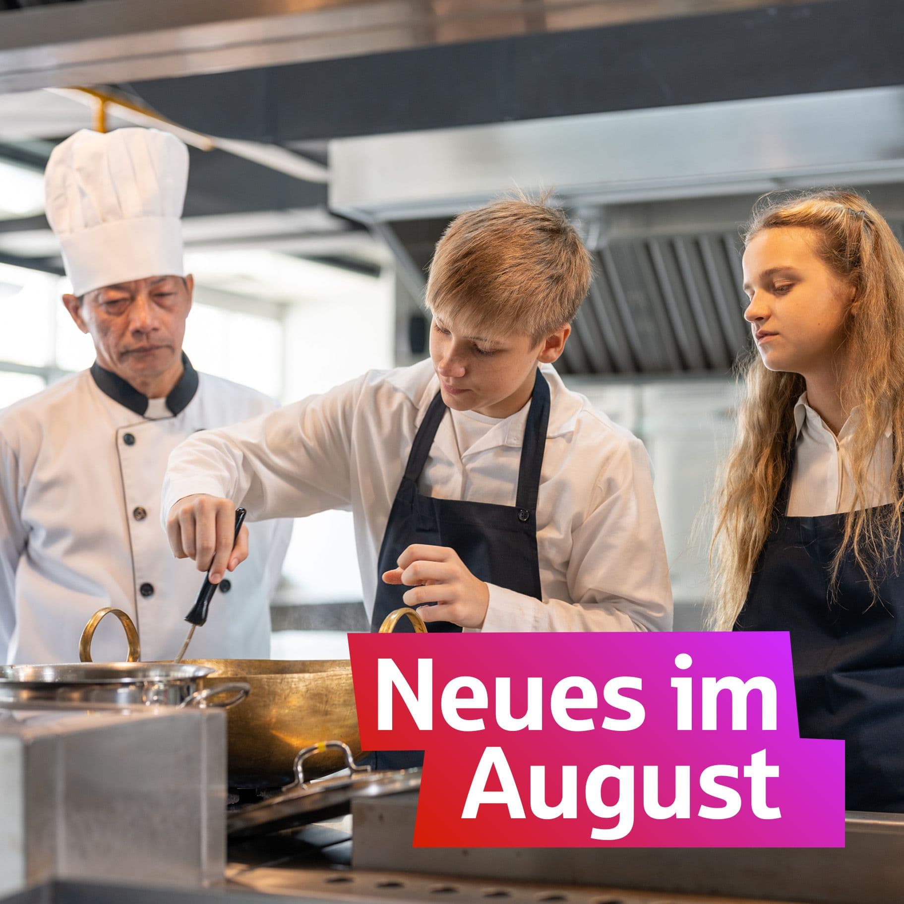 Jugendliche Azubis stehen in einer Küche. Neben Ihnen steht ein Koch, der sie ausbildet.