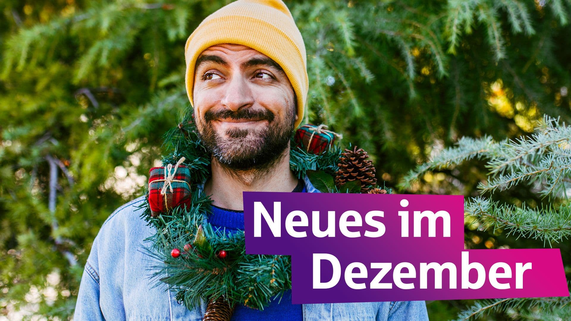 Ein Mann mit gelber Mütze grinst. Er hat einen Adventskranz um den Hals.