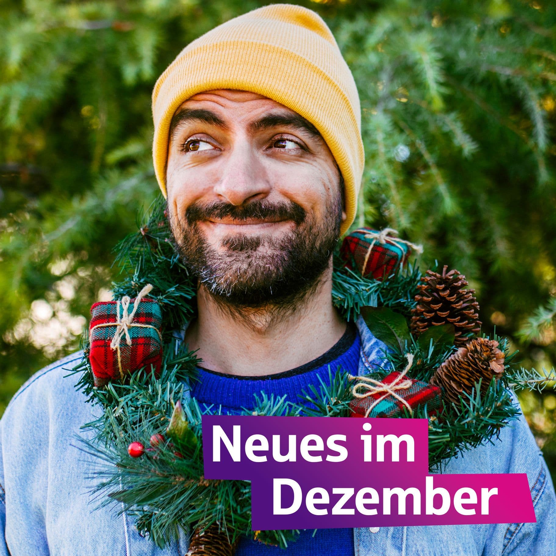 Ein Mann mit gelber Mütze grinst. Er hat einen Adventskranz um den Hals.
