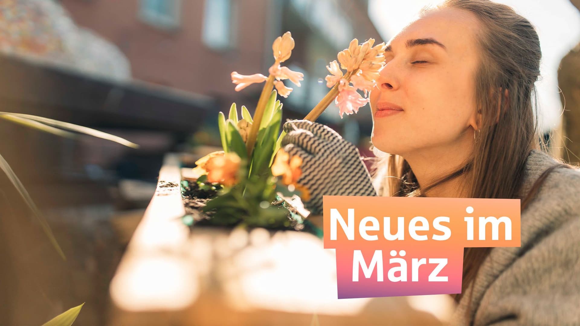 Frau steht auf einem Balkon und riecht an einer Blume während die Sonne scheint. Darüber steht in bunter Schrift Neues im März