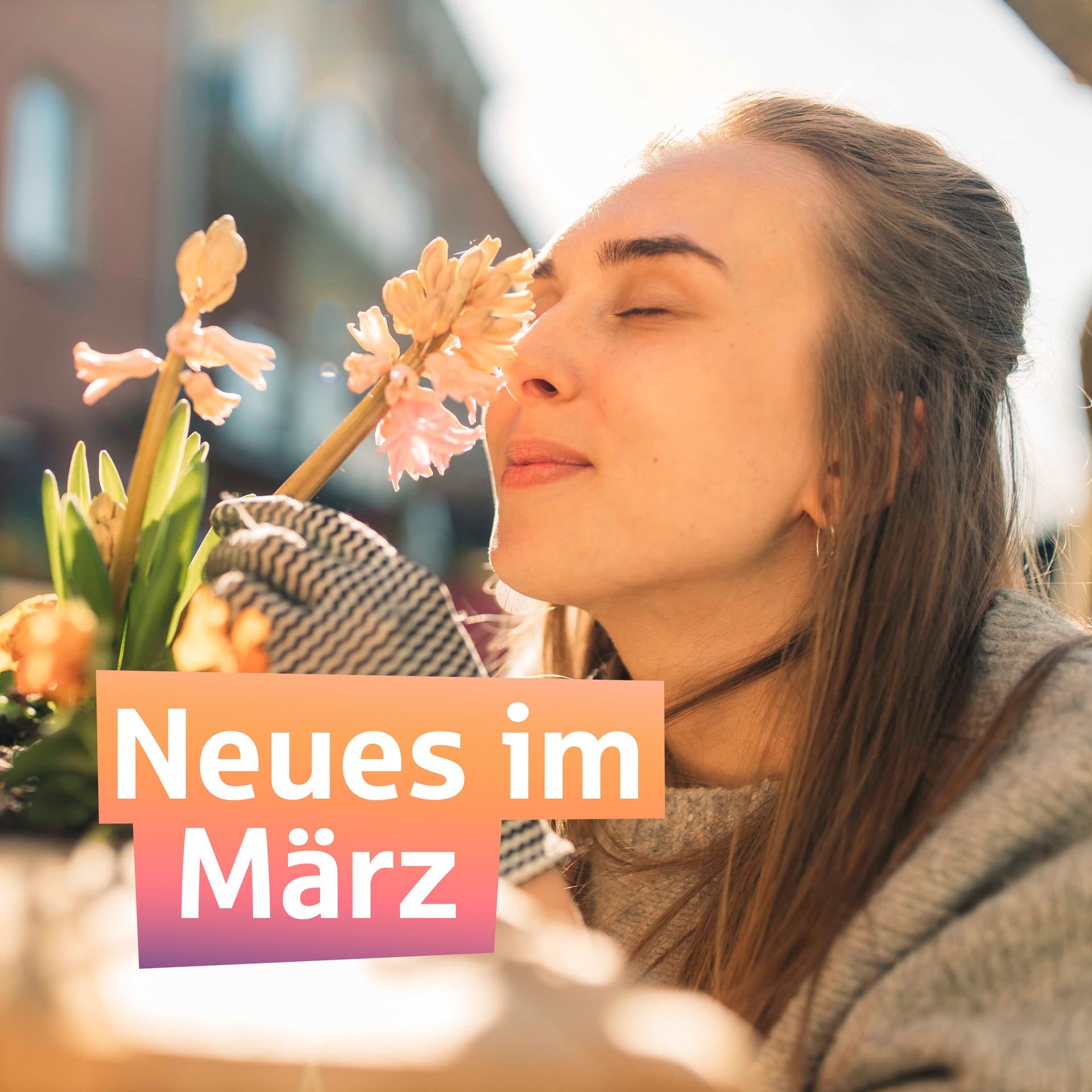 Eine junge Frau in beiger Strickjacke riecht an einer Hyazinthe, die sie sich mit einer Hand Richtung Nase zieht. Darüber der Schriftzug "Neues im März"