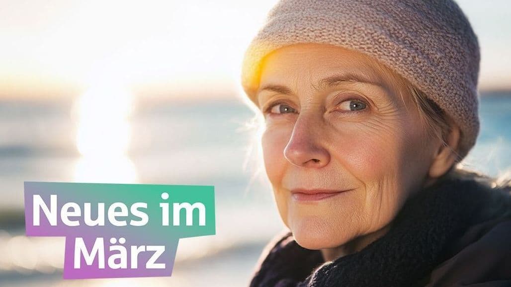 Eine ältere Frau steht vor dem Meer und schaut in die Kamera. Sie hat eine Mütze auf.