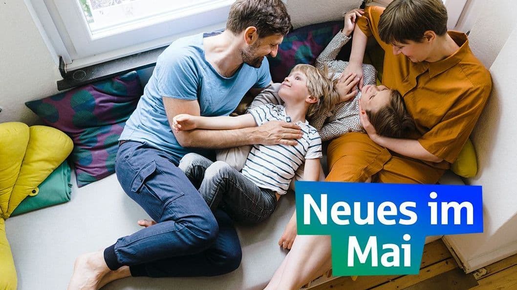 Eine Familie liegt kuschelnd auf ihrer Couch am Fenster.