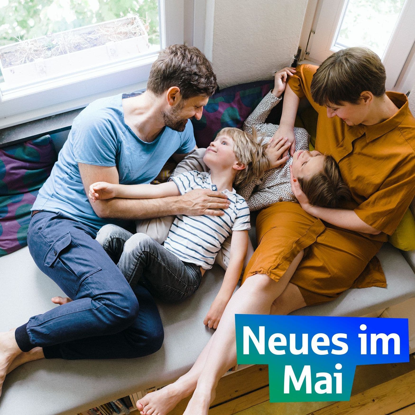 Eine Familie liegt kuschelnd auf ihrer Couch am Fenster.