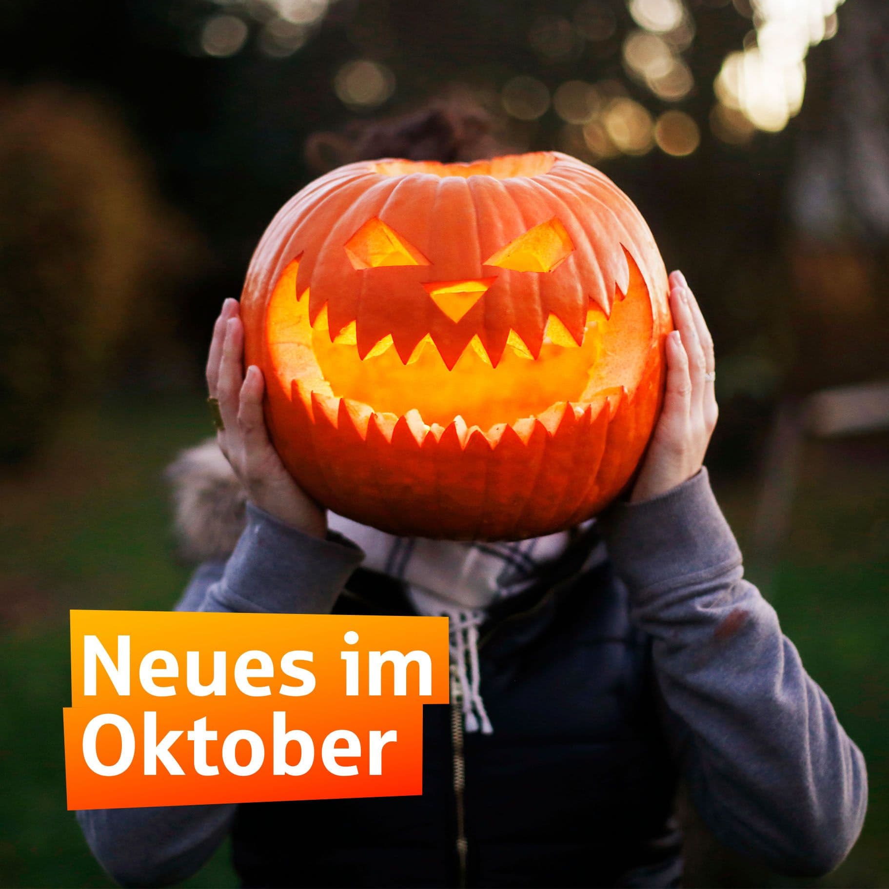 Eine Person hält in der Abenddämmerung draußen einen von innen leuchtenden Halloween-Kürbis vor ihr Gesicht.