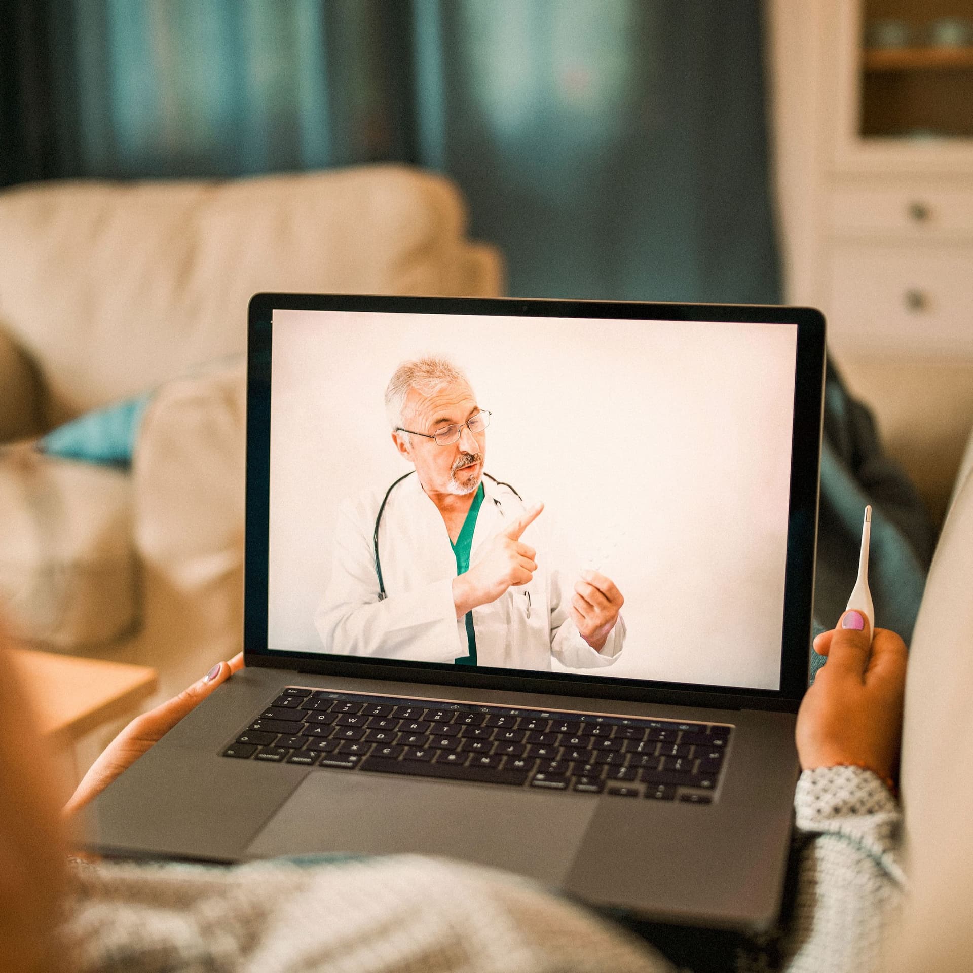 Eine kranke Frau führt ein Videogespräch mit einem Arzt. Sie hält ein Fieberthermometer in der Hand.
