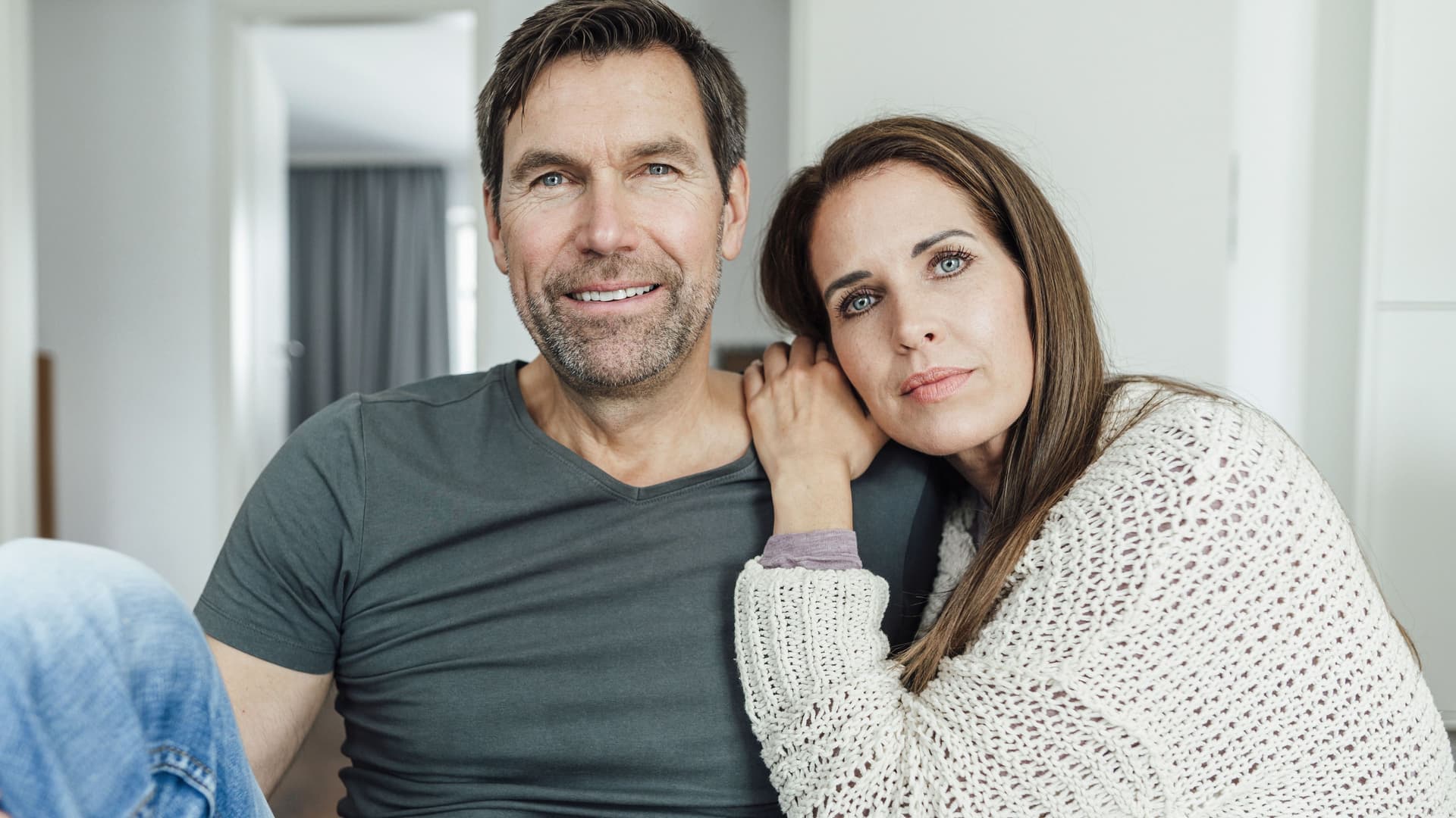 Mann und Frau sitzen zusammen auf einer Couch. Sie lehnt den Kopf an seine Schulter.
