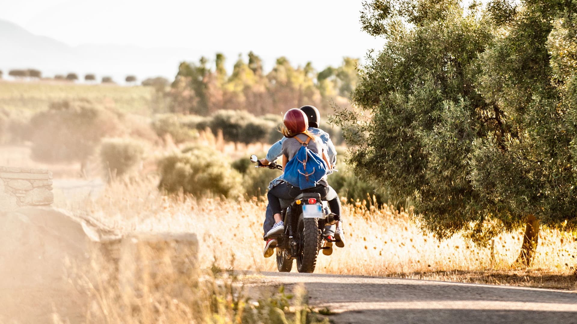 Rückansicht eines Paares beim Motorradfahren auf einer sonnigen Landstraße