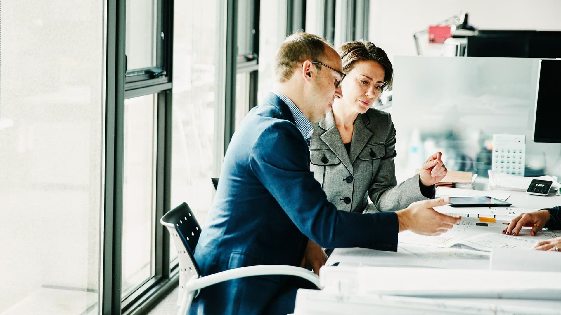 Drei Personen sitzen in einem modernen Büro an einem Tisch und besprechen gemeinsam Dokumente. Sie wirken konzentriert und professionell.