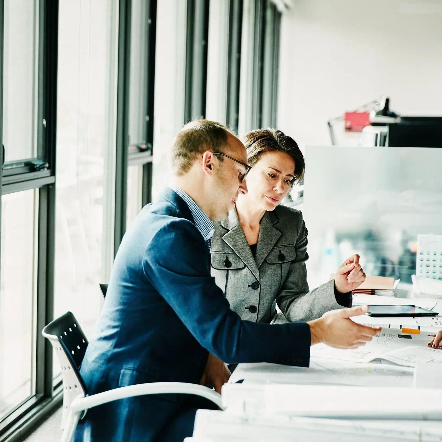 Drei Personen sitzen in einem modernen Büro an einem Tisch und besprechen gemeinsam Dokumente. Sie wirken konzentriert und professionell.
