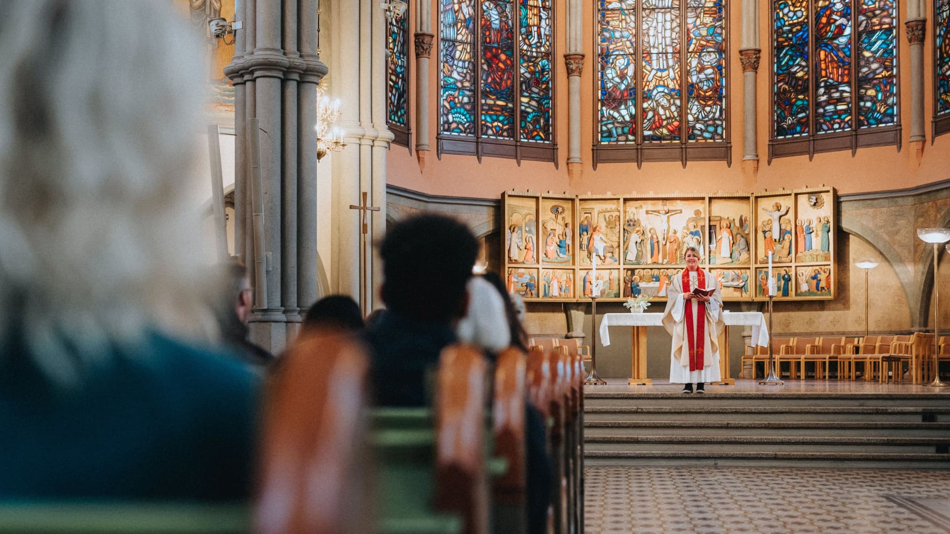 Pfarrerin in weißem Talar steht vor Altar und blickt auf die Gemeinde in der Kirche.