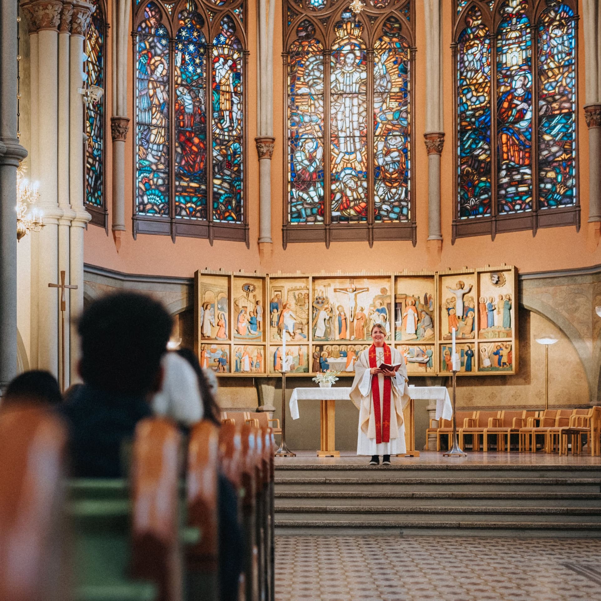 Pfarrerin in weißem Talar steht vor Altar und blickt auf die Gemeinde in der Kirche.