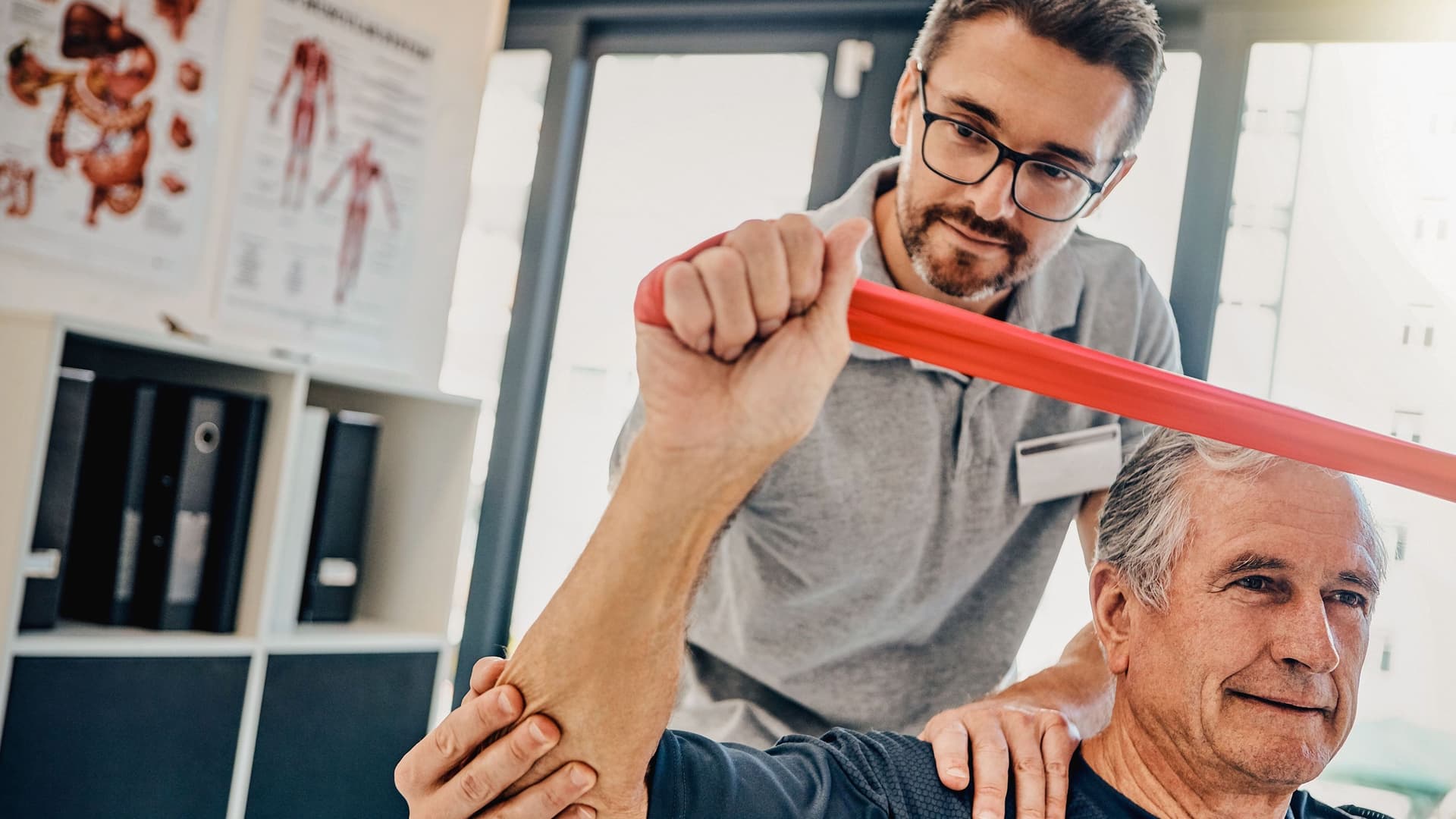 Ein Physiotherapeut hilft einem älteren Patienten, seine Arme mit einen Band zu strecken.
