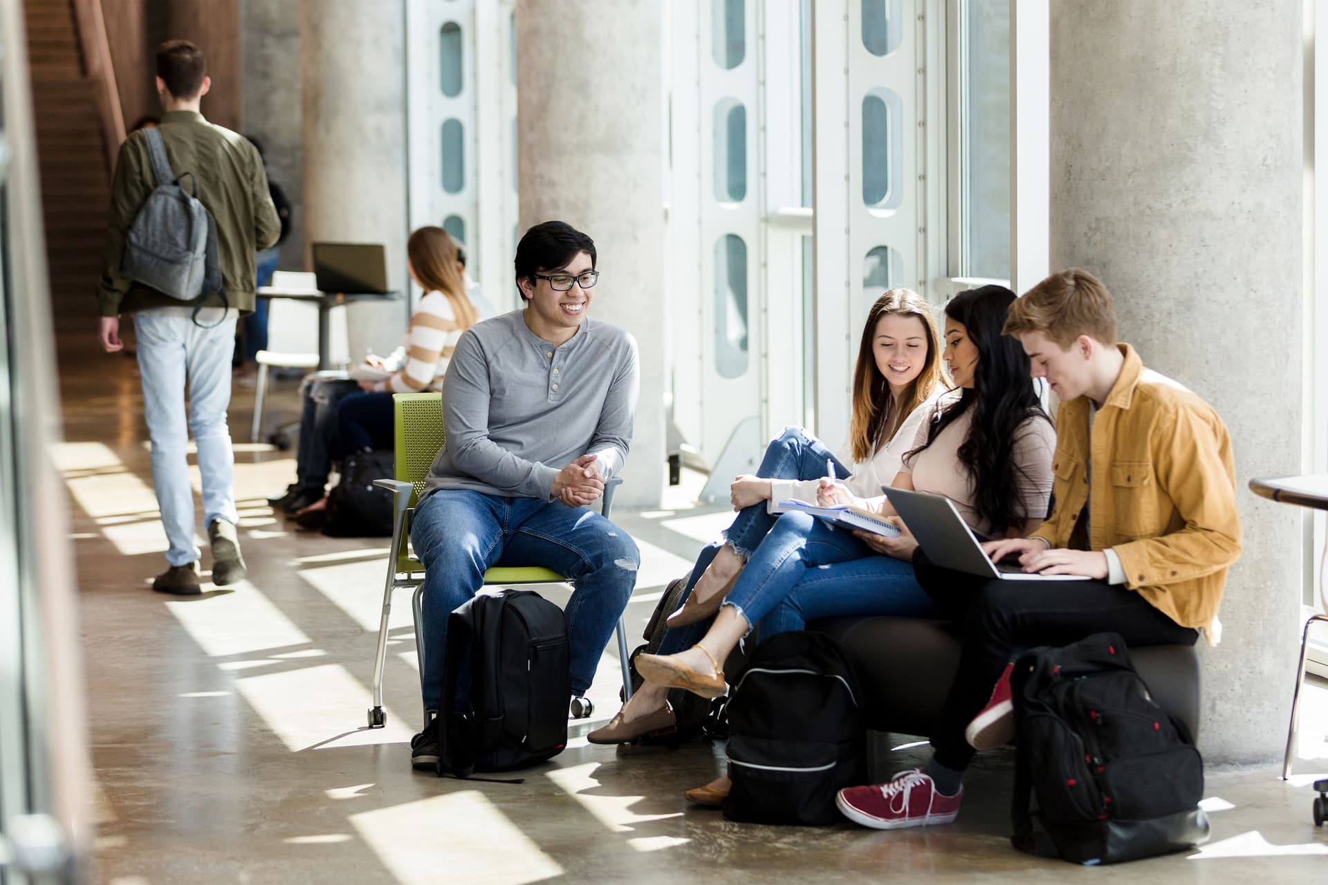 Eine Gruppe Jugendlicher sitzt auf Stühlen mit einem Laptop im Flur eines Schulgebäudes zusammen.