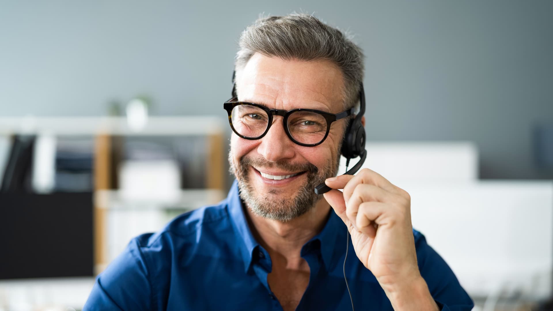 Porträt Mann mittleren Alters mit Headset der in die Kamera lächelt.
