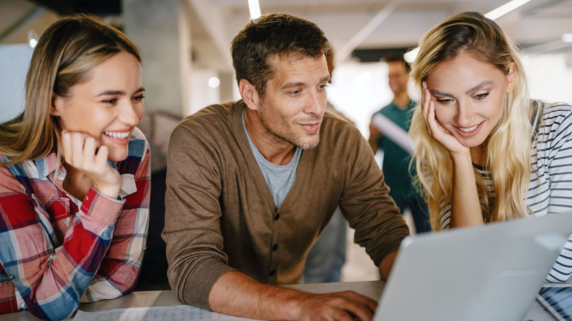 Gruppe von zwei Frauen und einem Mann betrachten ausgelassen einen Laptopbildschirm in einem Büro.