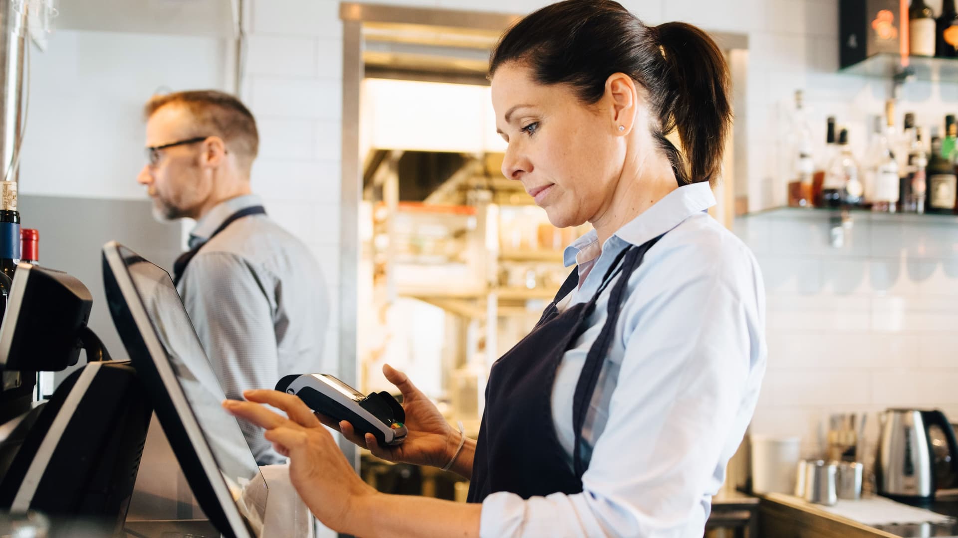 Besitzer, der Computer benutzt, während er Kreditkartenleser im Restaurant hält